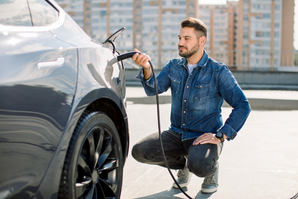 a man sitting down while holding the charger plug for an electric vehicle