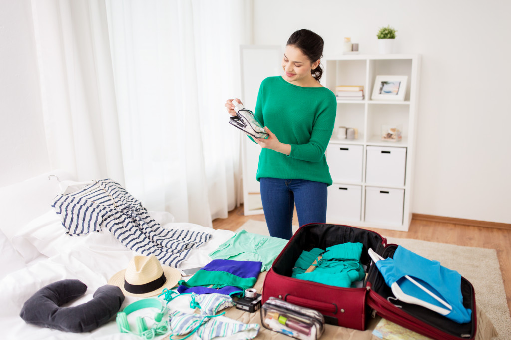 woman packing clothes into a red luggage on top of bed