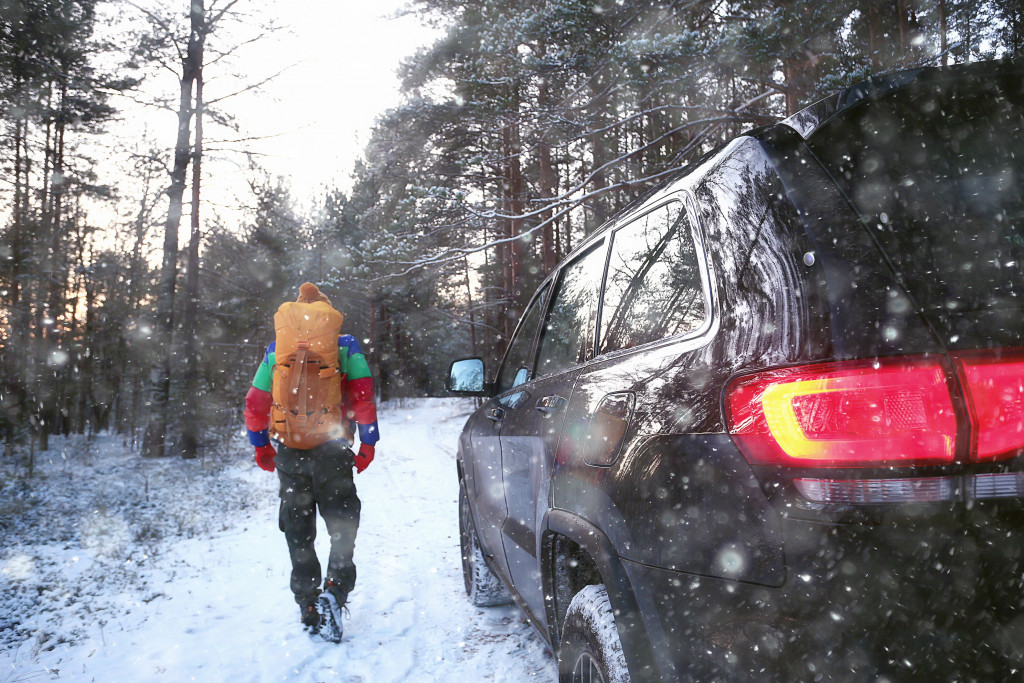 An SUV passes by a walking man in a forest full of snow