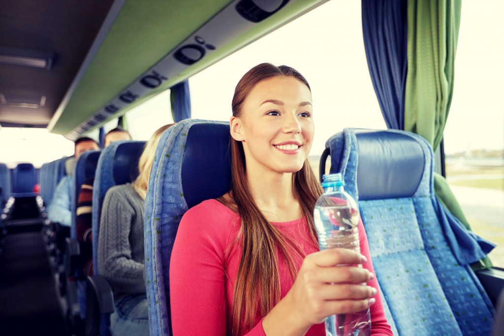 A tourist woman holding a bottled water while riding a bus