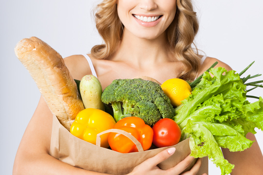woman smiling while holding paper bag with vegetables and fruits