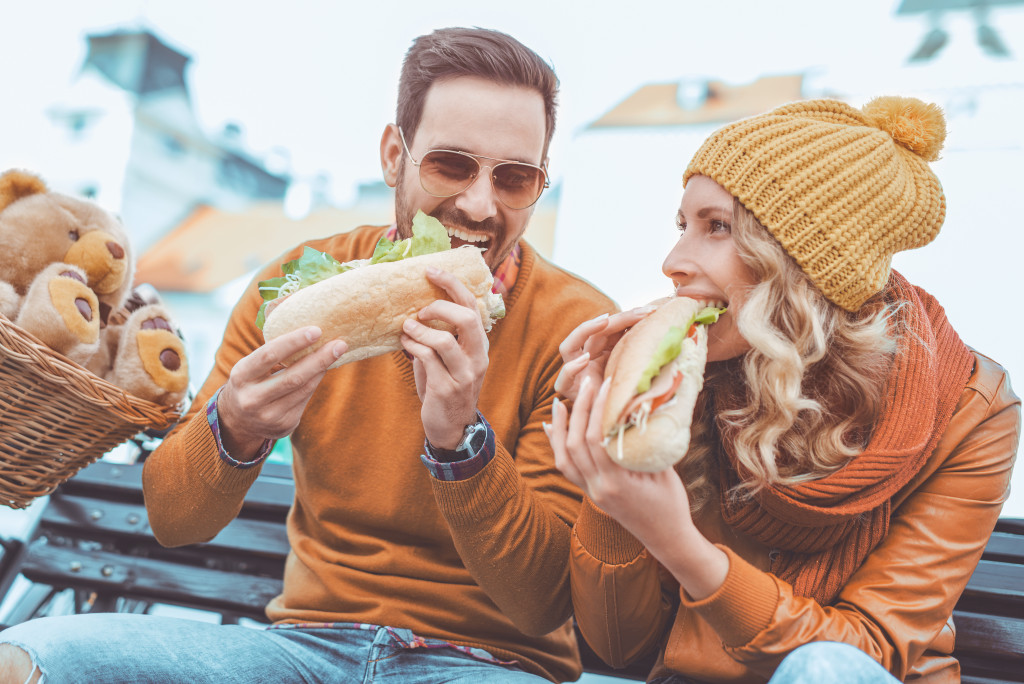 a man and woman eating sandwiches outdoors