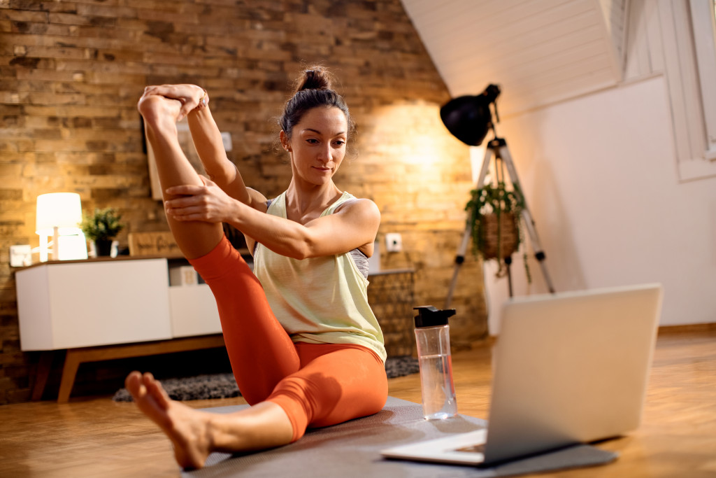woman stretching and working out at home in front of laptop