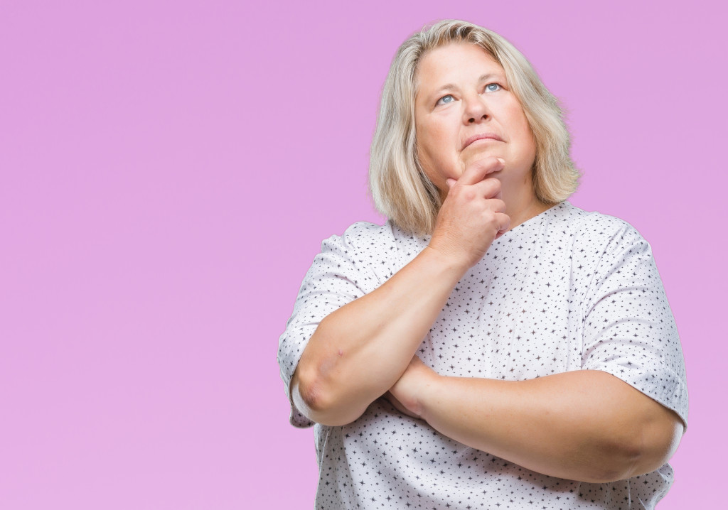 overweight woman in a pink background thinking