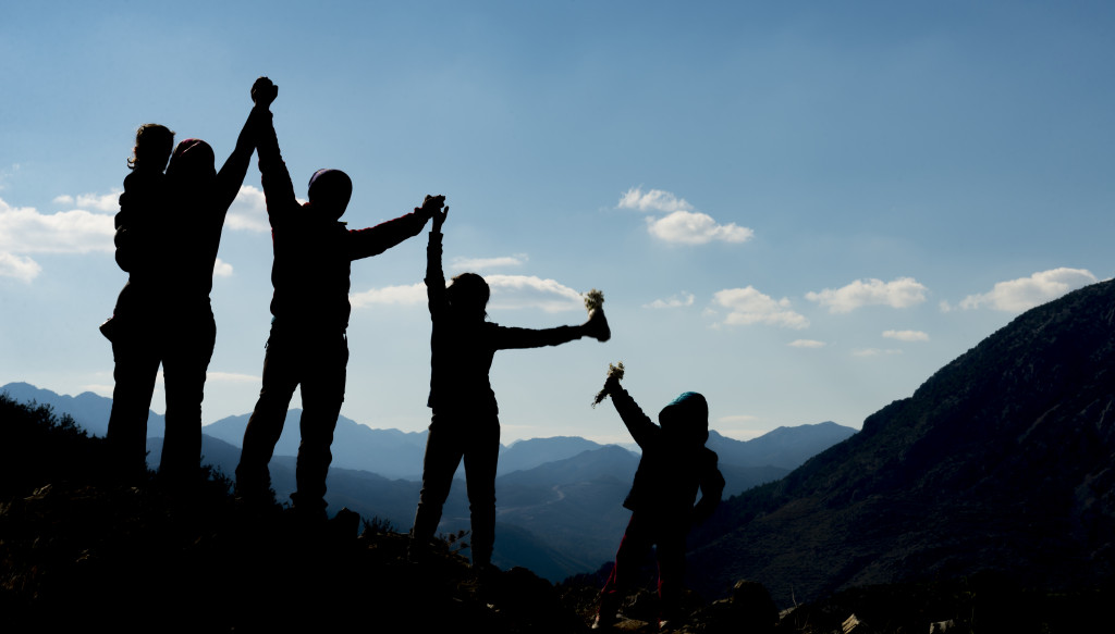 Silhouette of a family on a mountain with their arms raised.