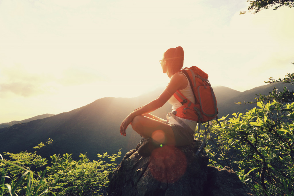Young woman sitting on a mountain peak while enjoying the sunrise.
