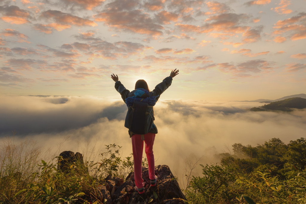 Young woman raising her arms during sunrise on a mountain peak.
